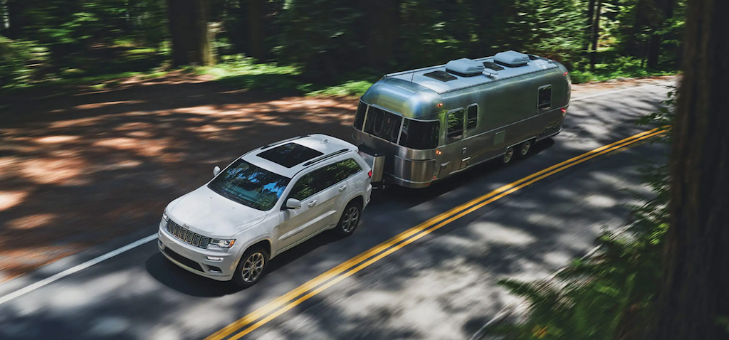 The 2021 Jeep Grand Cherokee towing a trailer in the woods.