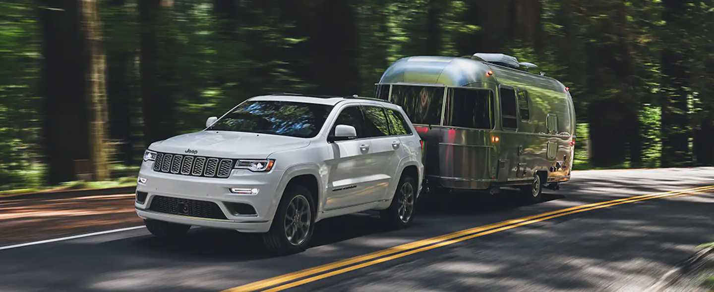 A Jeep Grand Cherokee towing a smaller trailer through an area like Huntington Beach and Long Beach.