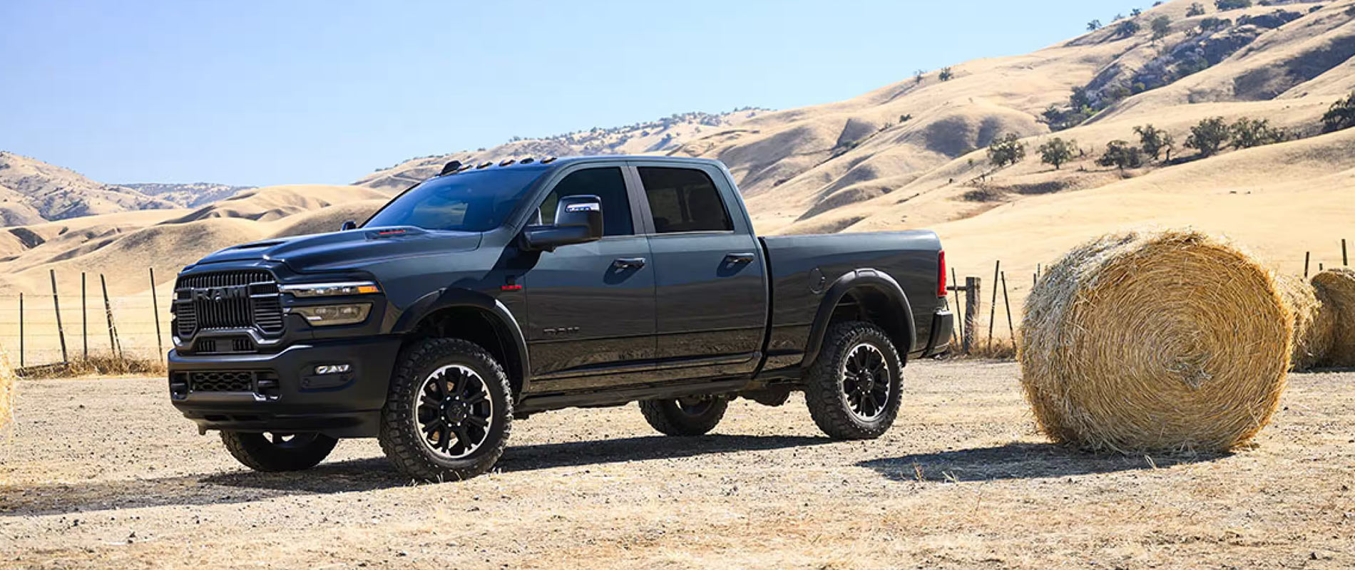 A black 2025 RAM 2500 parked on a desert ranch next to a hay bail
