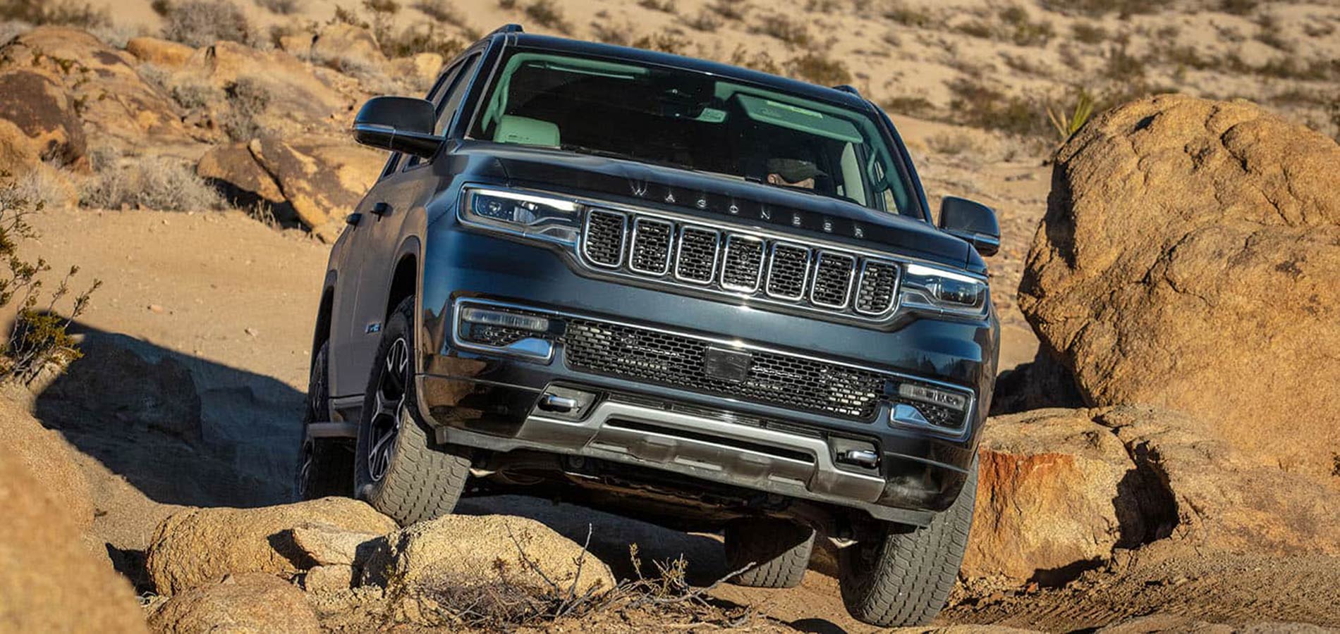 A dark blue Jeep Wagoneer driving off-road over rocks