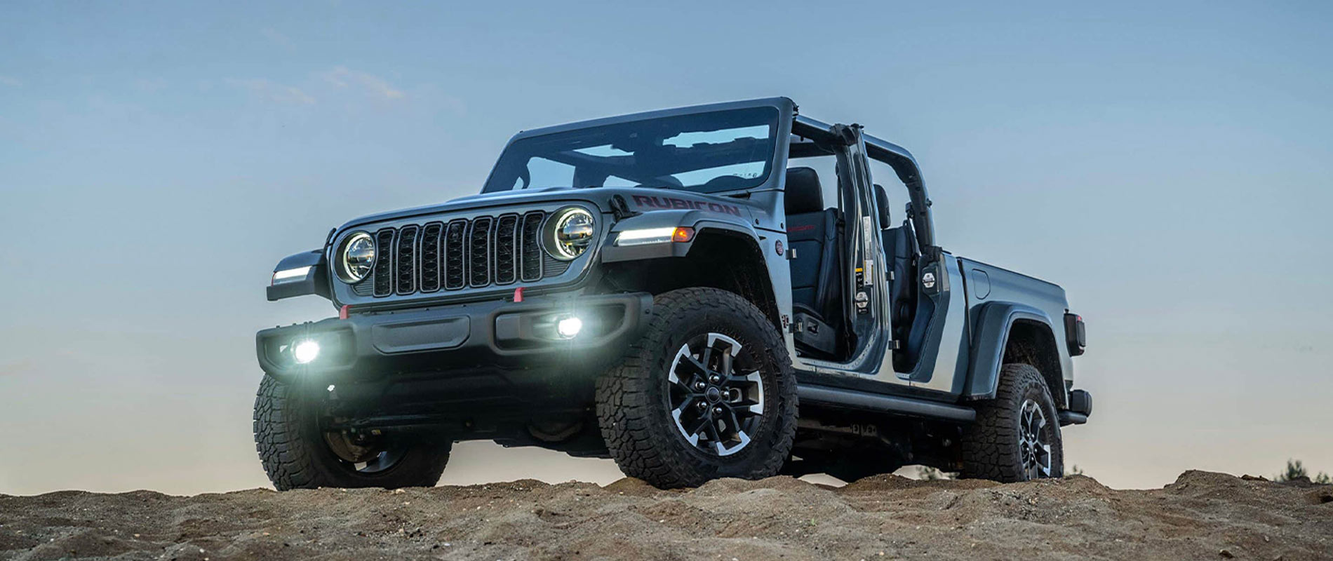 A blue 2026 Jeep Gladiator with its lights on at the top of a hill.