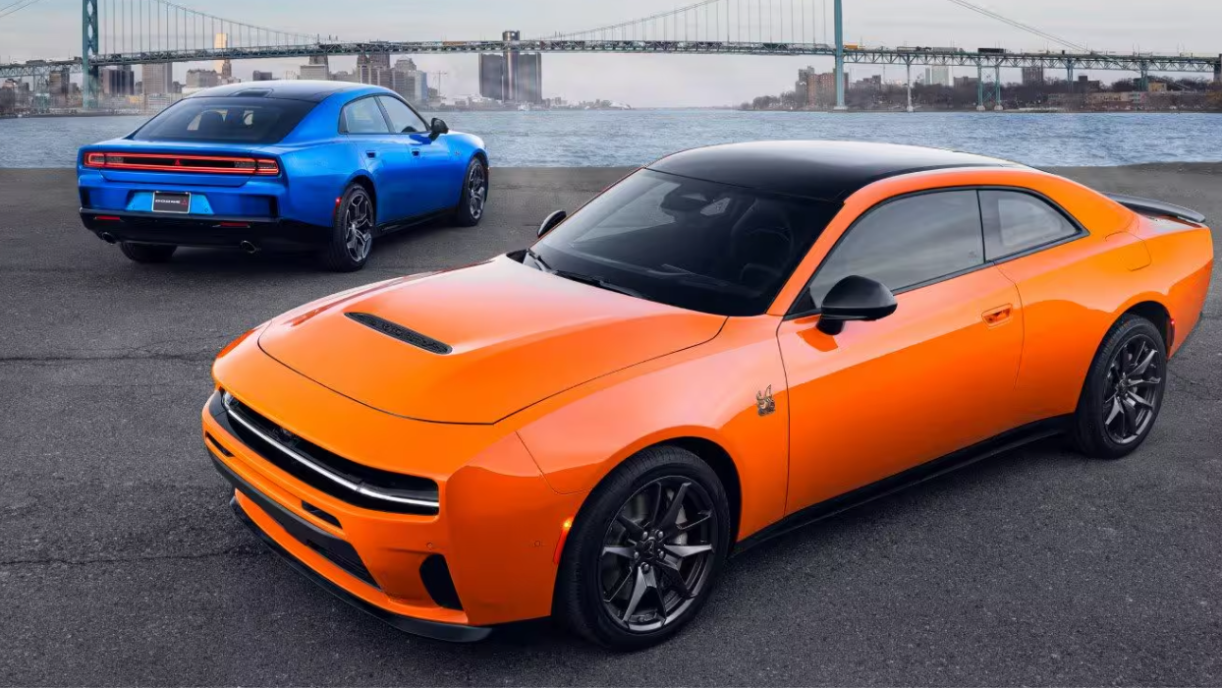 Two 2026 Dodge Charger models (one orange, one blue) parked in front of a bridge and body of water