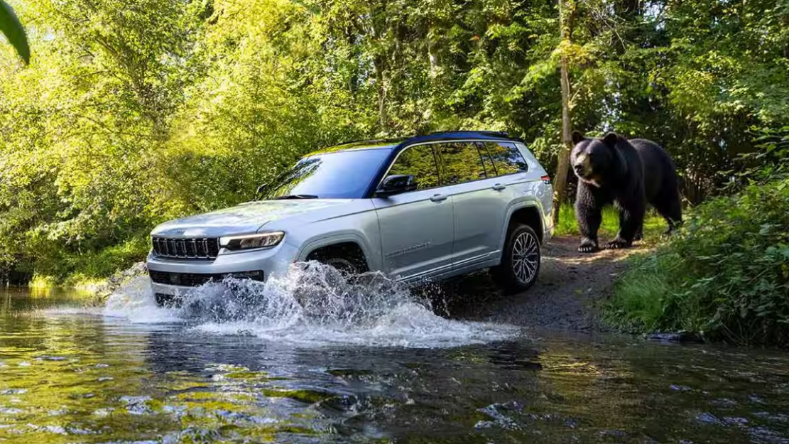 2026 Jeep Grand Cherokee entering shallow water with a bear behind it