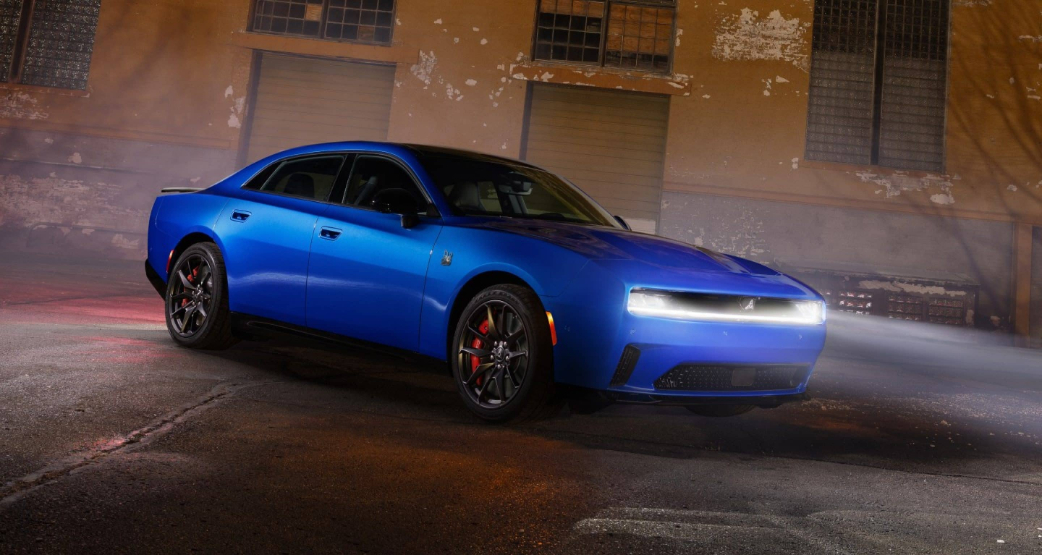 A blue Dodge Charger in a warehouse with its front lights on.