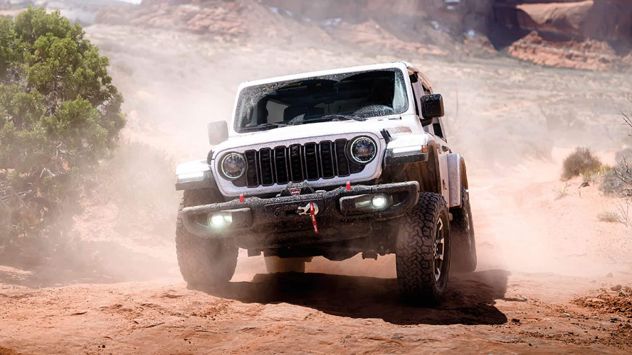 A white Jeep Wrangler kicking up dust as it drives off-road in a desert.
