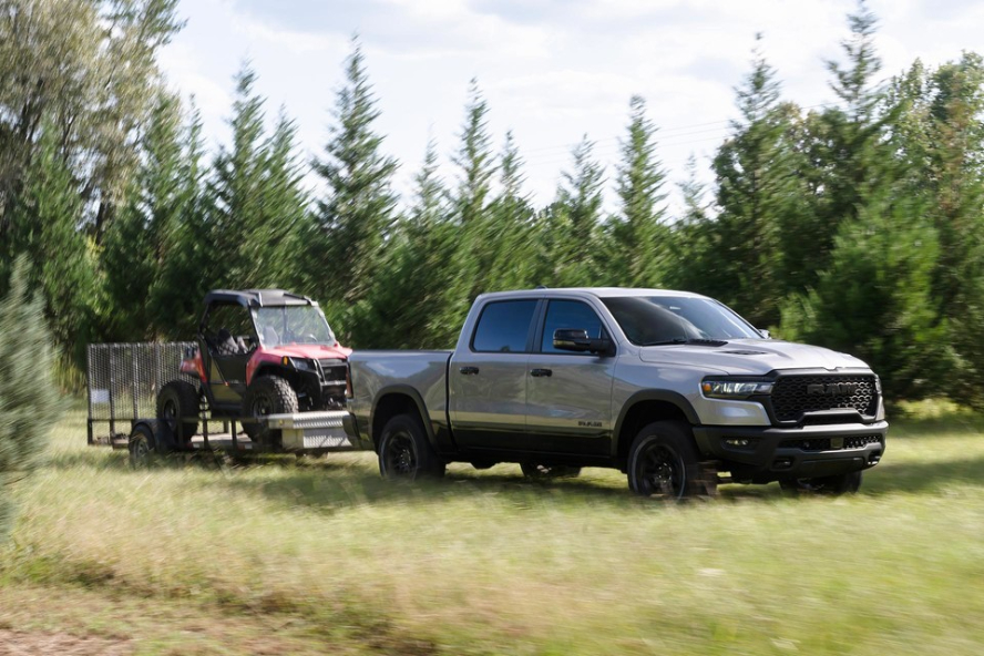A silver RAM 2500 driving off-road through a field while towing a trailer with a red work cart.
