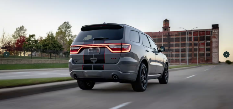A rear image of a grey Dodge Durango driving down the road towards a building.